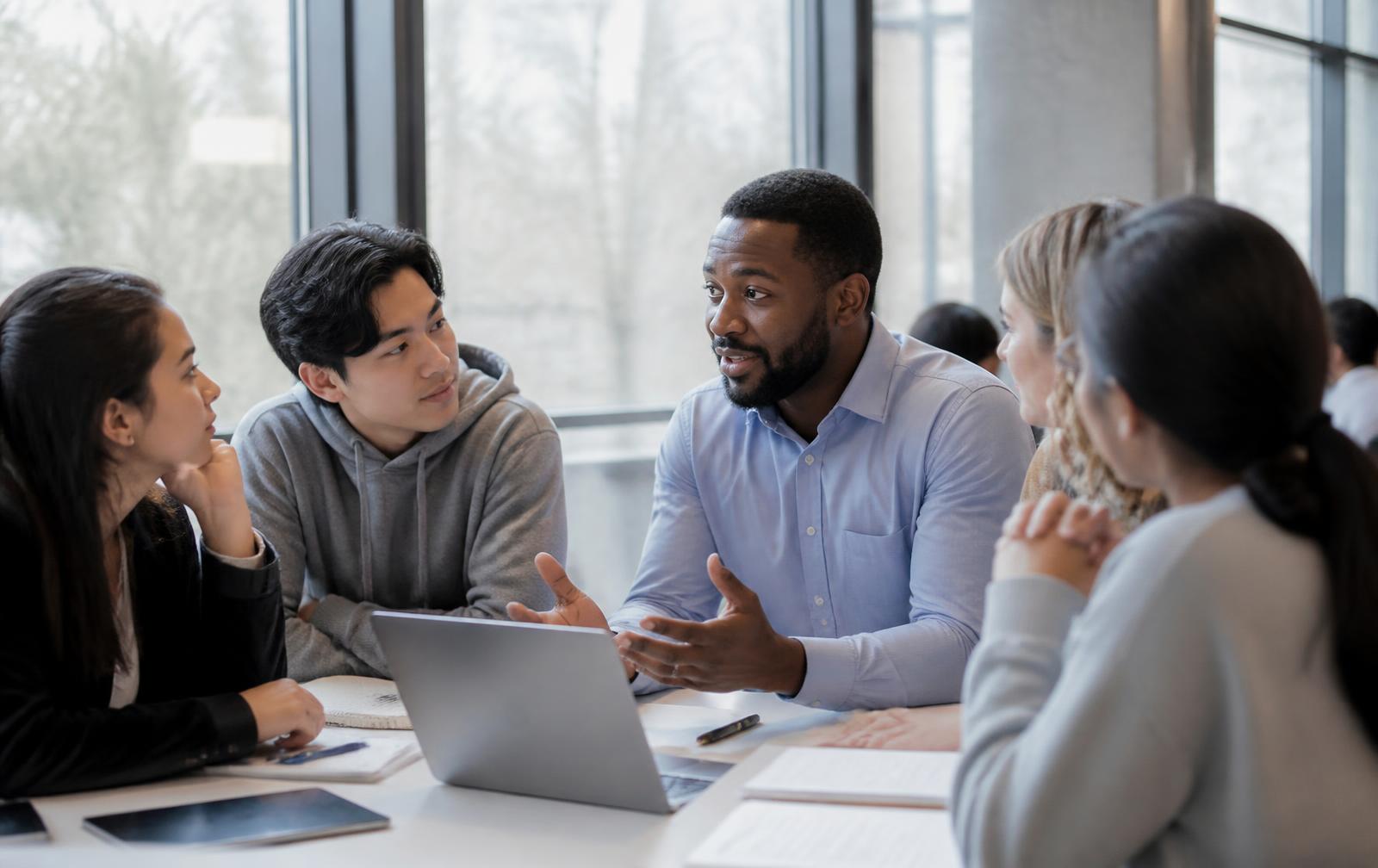A mentor talking with a group of young students around a table